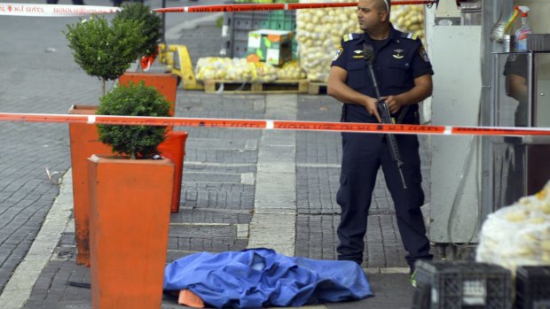 An Israeli policeman stands by the body of a Palestinian at the scene of a stabbing attack in Jerusalem.