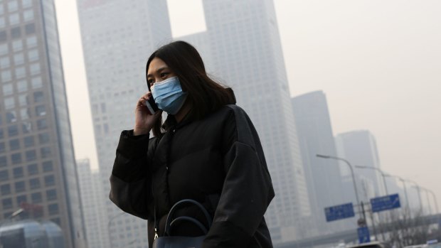 A woman wearing a mask to protect herself from pollutants walks past office buildings shrouded in haze in Beijing.