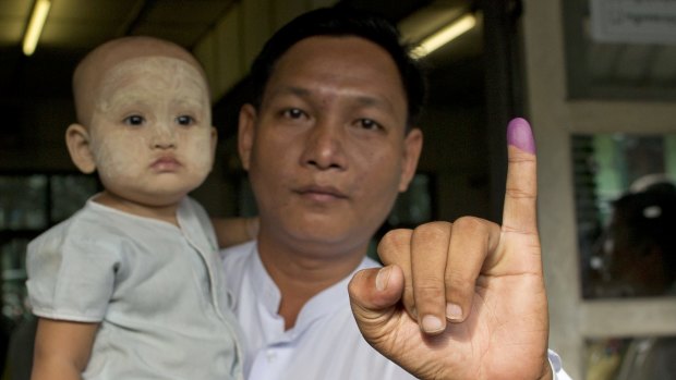 A man holding a child shows his finger marked with indelible ink after casting his vote in Yangon.