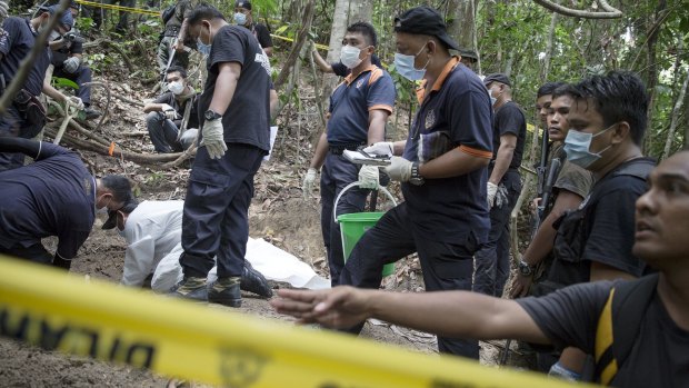 Policemen monitor as forensic experts dig out human remains near the abandoned human trafficking camp.