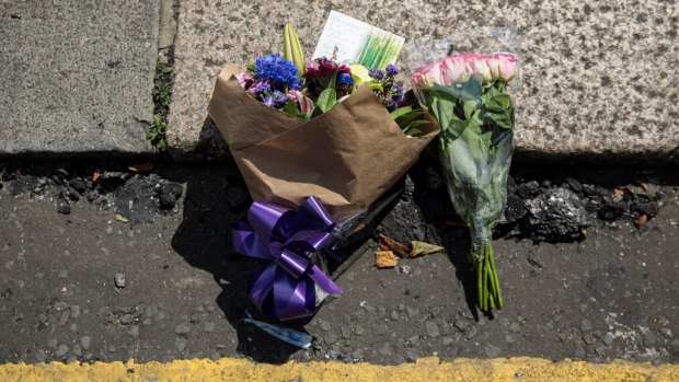 Floral tributes lie among burnt material near the scene of the burning 24 storey residential Grenfell Tower block in West London on June 14, 2017.
