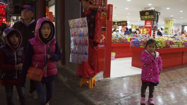 Children pass by a man dressed like an emperor, centre, promoting photography services in Beijing.