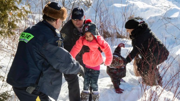 Asylum seeker children are helped into Canada by Royal Canadian Mounted Police officers along the US-Canada border near Hemmingford, Quebec, on Friday.