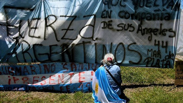 A woman sits in front of a banner blanketed with messages of support for the missing crew members of the ARA San Juan.