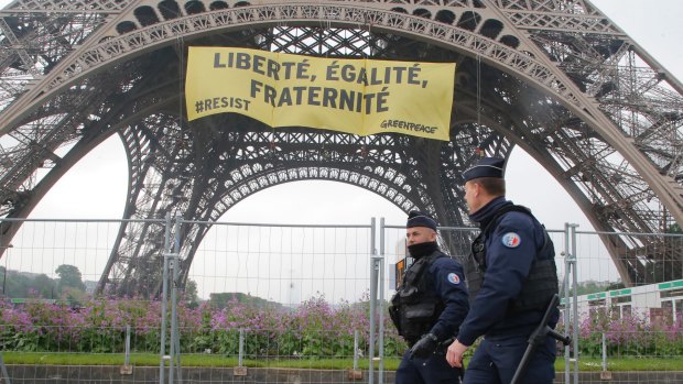 Police officers walk past the Eiffel tower as Greenpeace activists display a banner.