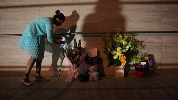 A young girl leaves flowers at the front of NSW Police Headquarters in memory of police employee Curtis Cheng.