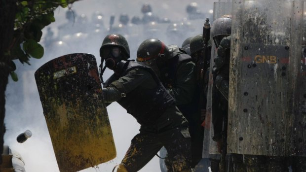 Bolivarian National Guards shield themselves from a jar of faecal matter flying towards them in Caracas on Wednesday.