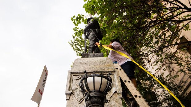 An unidentified protester climbs a ladder to place a rope around a Confederate statue during a rally on Monday.
