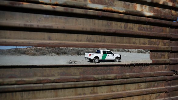 A Border Patrol vehicle drives by in Tecate, California, seen through a hole in the metal barrier that lines the border.