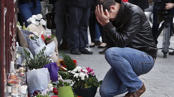 Grief stricken: A man lays flowers at the scene of one of the attacks, in front of the Carillon cafe, in Paris. 