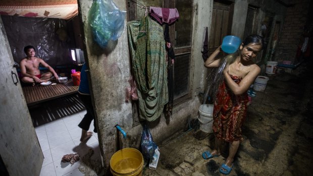 Poor Cambodia: A woman washes herself outside a tiny room where she lives with four other family members off a dank alleyway near the Phnom Penh factory where she works. 