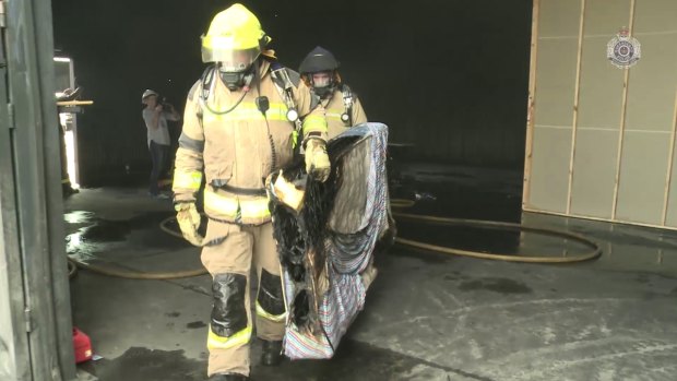 Firefighters remove a mattress burnt in a reconstruction of the house fire at Morayfield as part of an investigation into the suspected murder of two kids and attempted murder by arson of two others. 