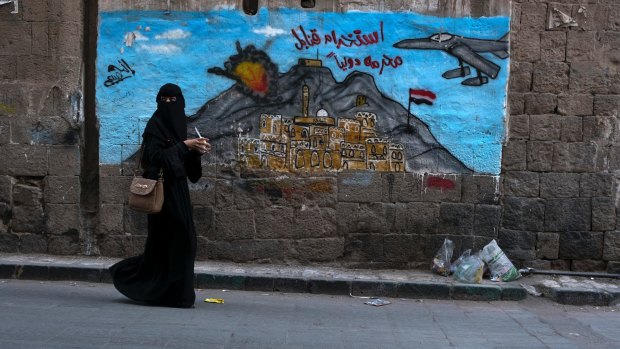A woman passes a mural depicting airstrikes in Sanaa, Yemen.