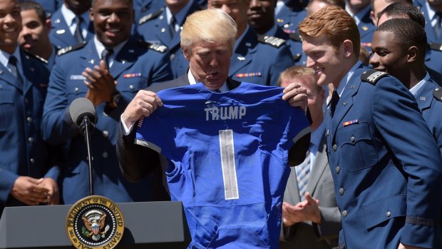 President Donald Trump holds up a football jersey presented to him at a US Air Force Academy commander-in-chief trophy presentation.