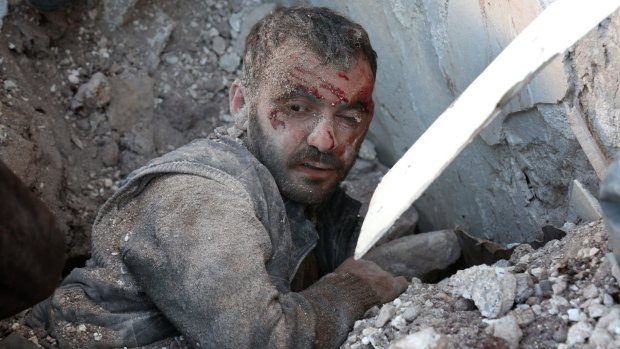 A wounded man is trapped under the wreckage of collapsed buildings after air strikes on residential areas near Aleppo.