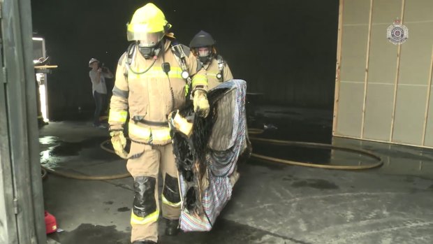 Firefighters remove a mattress burnt in the reconstruction of the house fire.