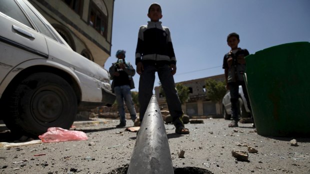 Boys stand in front of a partially-buried artillery shell in Sanaa.