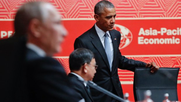 Barack Obama takes his seat at the APEC table, beside Thai Deputy Prime Minister Prajin Juntong while Vladimir Putin looks straight ahead.