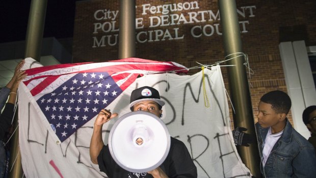 A protester chants in front of a flag which reads "racism lives here" outside the Ferguson police department building.