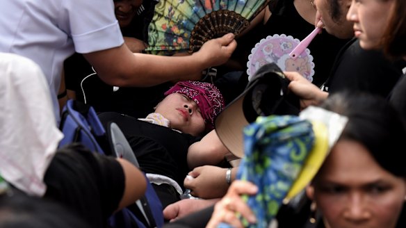 A woman faints outside the Grand Palace in Bangkok while waiting for the body of King Bhumibol to arrive.