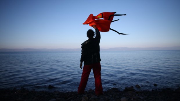 A woman waves a life jacket to direct a migrant boat ashore as it makes the crossing from Turkey to the Greek island of Lesbos.