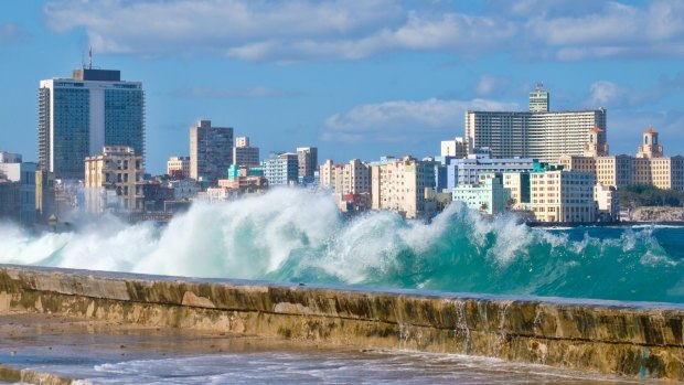 The Havana skyline with waves crashing on the Malecon seawall.