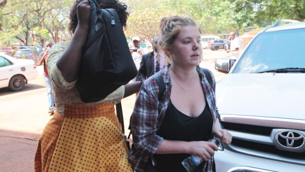 Martha O' Donovan, right, arrives at court in Harare with a plain clothes police officer shielding her face.