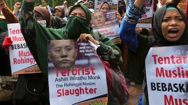 Muslim women, holding a poster depicting Wirathu, the leader of Myanmar's nationalist Buddhist monks, raise their fists outside Myanmar Embassy in Jakarta, Indonesia.