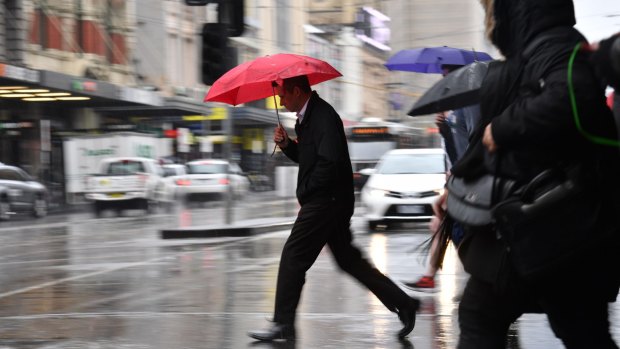 The rain falls on pedestrians crossing Flinders Street on Tuesday.
