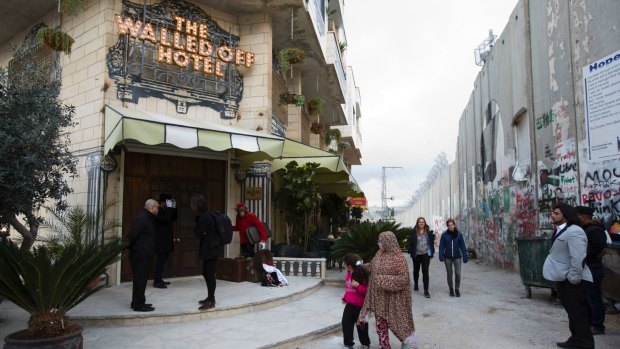 People pass the Walled Off Hotel and the wall in Bethlehem, in the Israeli-occupied West Bank.