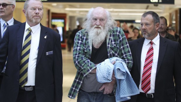 Colin Michael Newey is escorted through Sydney Airport by police after being extradited from South Australia.