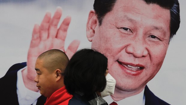 A masked woman and a man walk by a poster of Chinese President Xi Jinping on a street in Beijing.