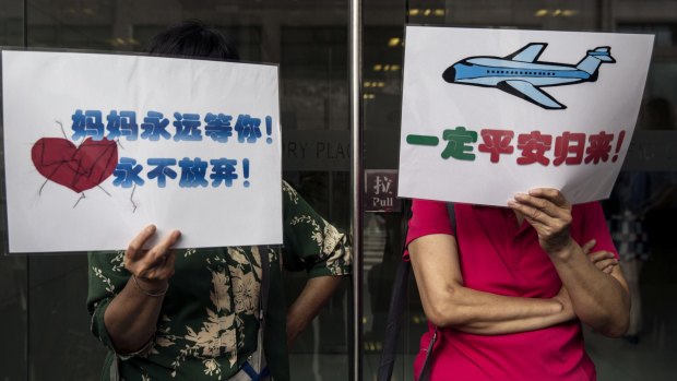 Chinese relatives of missing passengers  hold signs, one reading "Mama waits for you, Never Give Up", left, and "Must Come Back Safely", right, as they wait for updates outside the airline's office in Beijing.