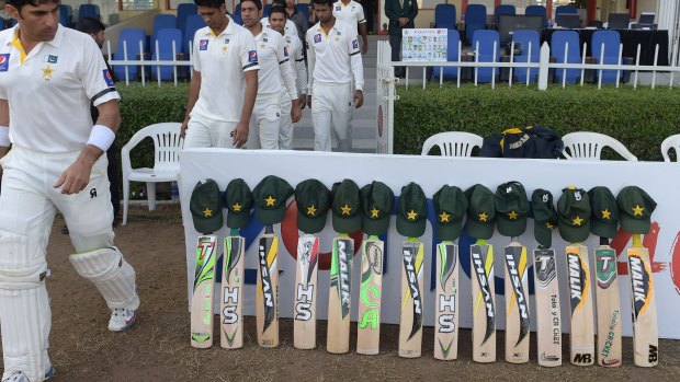 Pakistani cricketers walk past bats and caps placed outside the Pakistani dressing room ahead of the third day of the Test with New Zealand in Sharjah.
