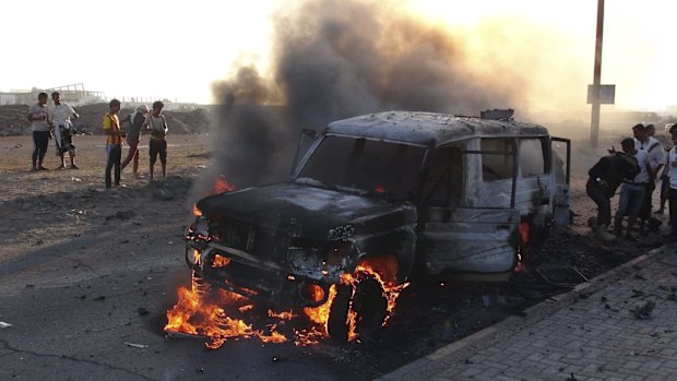 People watch a vehicle which belonged to Houthi rebels burn during clashes in the southern port city of Aden.