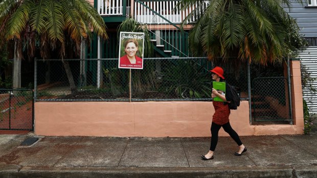 Greens candidate for South Brisbane Amy MacMahon walks past a corflute of Deputy Queensland Premier Jackie Trad.