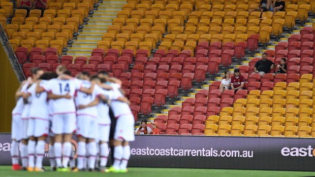 Empty feeling: Adelaide players huddle before a vacant-looking stand at Suncorp Stadium.