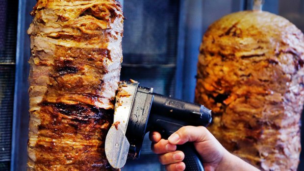 A man slices cuts of meat from a rotisserie Doner spit inside a Doner restaurant cafe in Frankfurt, Germany. 