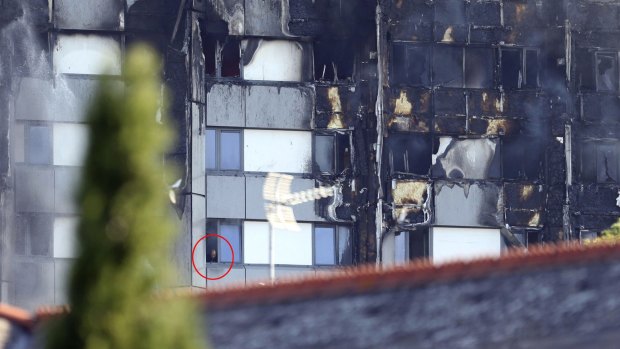 A man looks from a window of Grenfell Tower, as a fire burns three floors above him.