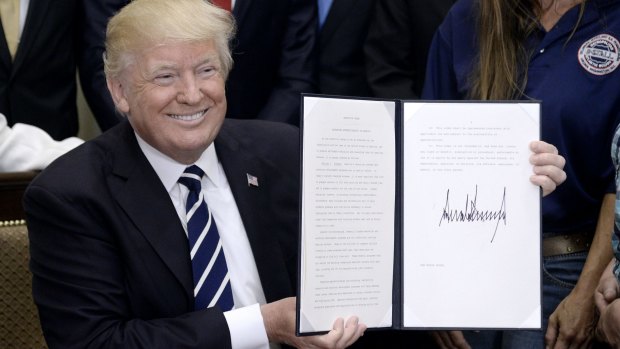 President Donald Trump holds up a signed executive order giving businesses expanded authority to design their own apprenticeship programs.