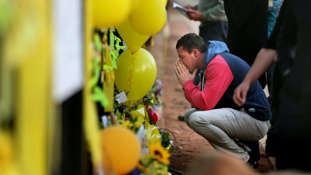 Stephanie Scott's fiance Aaron Leeson-Woolley reads messages at the floral memorial on the gates of the Leeton High School.