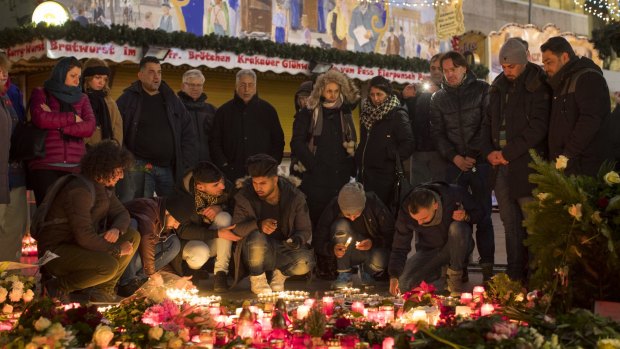 People light candles as floral tributes sit in Berlin Christmas market in Berlin days after a terror attack in December.