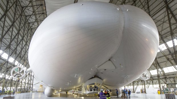 Workers and media stand under the front of the hull of the Airlander 10 in Bedford, Britain. 