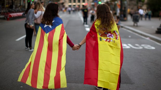Two Spaniards wearing a Spanish flag and a Catalan independence flag, walk along the street in Barcelona.
