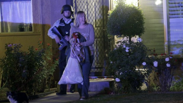 A police officer escorts a woman from a home as the search for a gunman continued. 