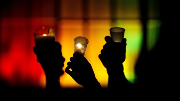 People hold up candles against a rainbow lit backdrop during a vigil for those killed in a mass shooting at the Pulse nightclub.