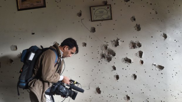 A Pakistani camera man shoots video in front of a bullet-riddled wall at the arm- run school a day after an attack by Taliban militants in Peshawar.