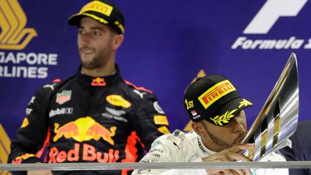 Mercedes driver Lewis Hamilton kisses his trophy after winning the Singapore Formula One Grand Prix with Red Bull driver Daniel Ricciardo looking on.