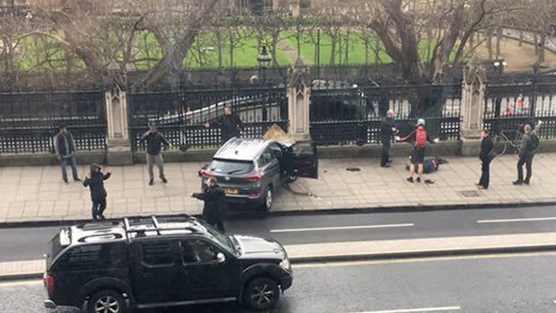 People stand near a crashed car and an injured person lying on the ground, right, on Bridge Street near the Houses of Parliament in London on Wednesday.