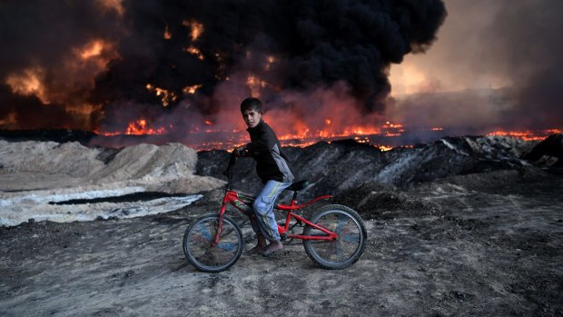 A boy pauses on his bike as he passes an oil field that was set on fire by retreating IS fighters ahead of the Mosul offensive in Qayyarah, Iraq. 
